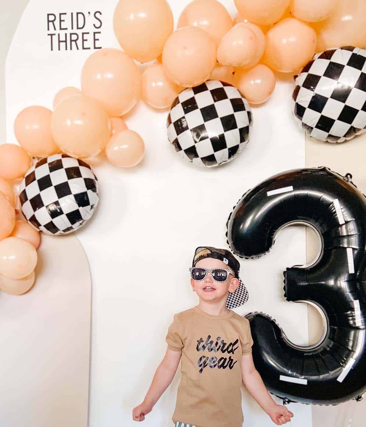 Modern race car birthday party with checkered balloon garland and tan wood backdrop